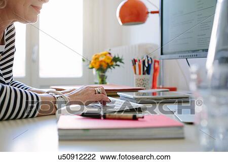 Stock Image - Close up of mature woman at home using computer. Fotosearch