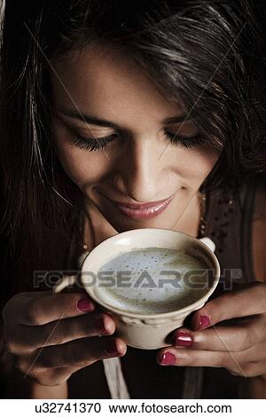Stock Image - Close up of young woman looking down at coffee cup. Fotosearch