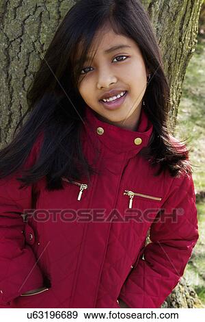 Stock Photo - Close up portrait of girl leaning against tree trunk. Fotosearch