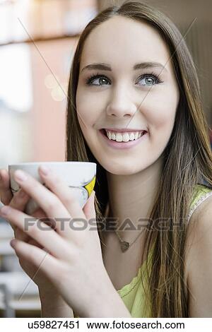 Stock Image - Close up portrait of young woman drinking coffee in cafe. Fotosearch