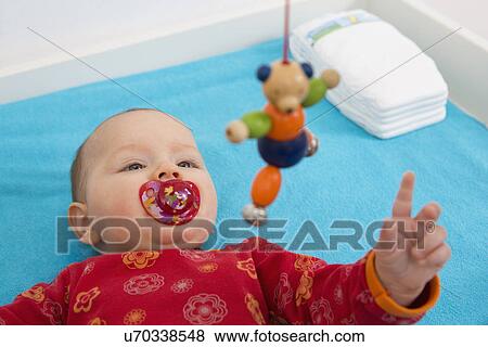 Stock Photo - Contented 7 month old baby girl playing with dangling teddybear. Fotosearch