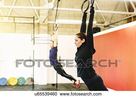 Stock Image - Couple pulling suspended rings in gym. Fotosearch
