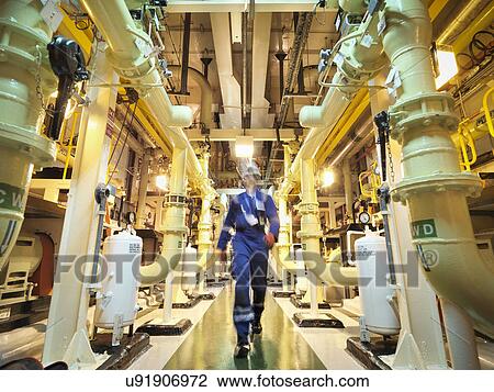 Stock Image - Engineer walking amongst pipes of nuclear power station. Fotosearch