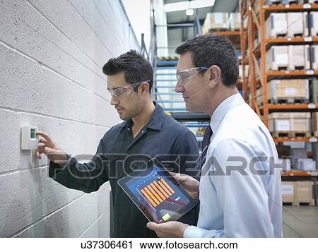 Stock Image - Factory and office workers checking thermostat in factory. Fotosearch