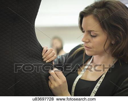 Stock Photo - Fashion designer adjusting garment in fashion design studio. Fotosearch