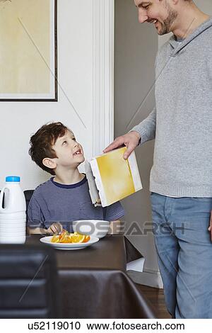 Stock Image - Father pouring cereal into son's bowl. Fotosearch