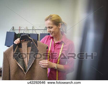 Stock Photograph - Female worker inspecting jacket in clothing factory. Fotosearch