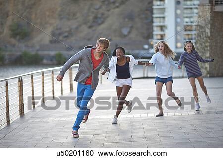 Stock Image - Four young adult friends running and holding hands. Fotosearch