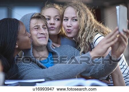 Stock Photo - Four young adult friends taking self portrait on smartphone. Fotosearch