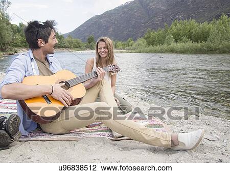 Friends sitting beside river, playing guitar View Large Photo Image Stock Image - Friends sitting beside river, playing guitar. Fotosearch