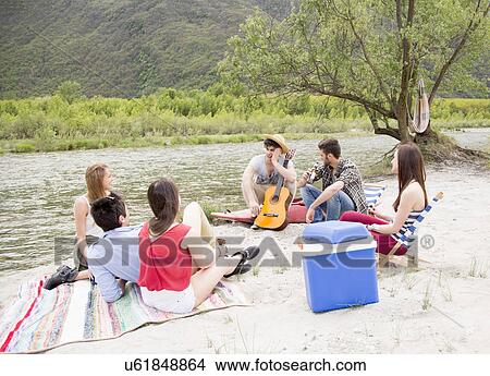 Friends sitting by river, playing guitar View Large Photo Image Picture - Friends sitting by river, playing guitar. Fotosearch