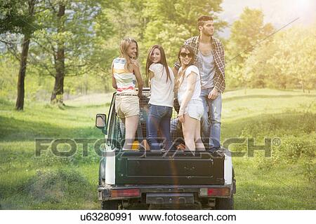 Stock Image - Friends standing on back of off road vehicle. Fotosearch