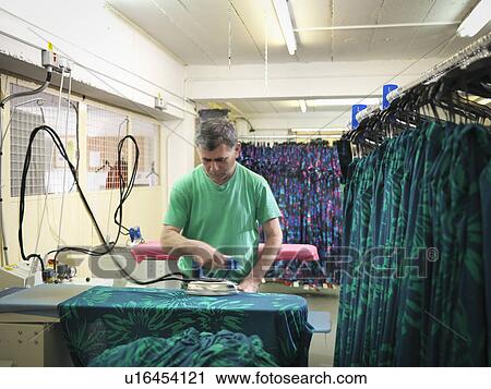 Stock Image - Garment worker ironing clothing in clothing factory. Fotosearch