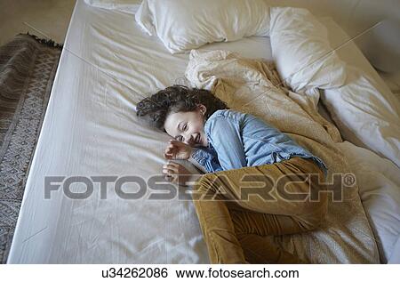 Stock Photograph - Giggling young girl curled up on bed. Fotosearch