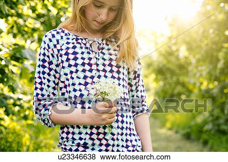 Stock Photo - Girl daydreaming whilst looking at bunch of wildflowers. Fotosearch