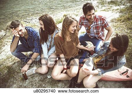 Stock Image - Group of five friends sitting on canoe on riverbank. Fotosearch