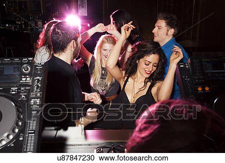Stock Image - Group of friends dancing in front of DJ in nightclub. Fotosearch