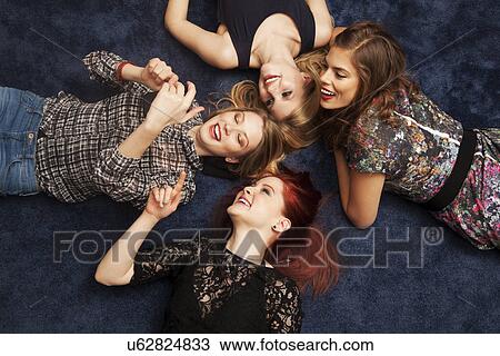 Stock Image - Group of friends lying on carpeted floor. Fotosearch
