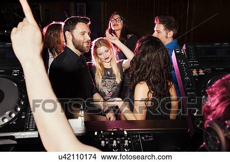 Picture - Group of young men and women dancing in front of DJ in nightclub. Fotosearch