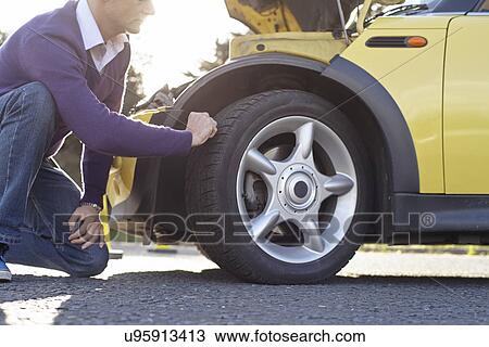 Stock Image - Man inspecting car tyre. Fotosearch