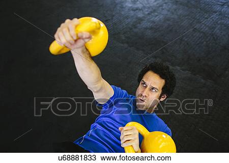 Stock Image - Man on back lifting kettlebells. Fotosearch