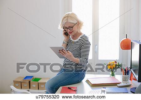 Mature woman at home using digital tablet and talking on phone View Large Photo Image Stock Image - Mature woman at home using digital tablet and talking on phone. Fotosearch