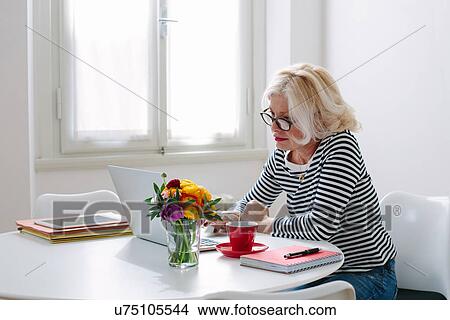 Picture - Mature woman at home using laptop. Fotosearch