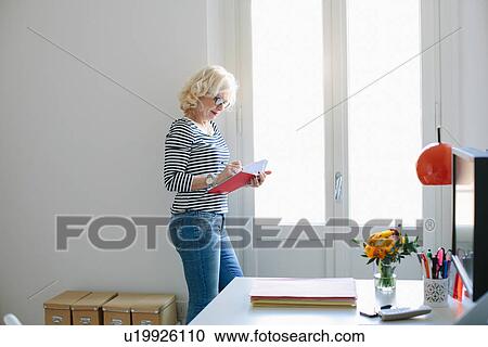 Stock Image - Mature woman at home writing in notebook. Fotosearch