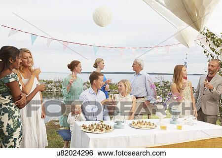 Stock Photograph - Mid adult couple making a toast with friends at wedding reception. Fotosearch