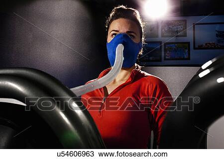 Stock Image - Mid adult female with face mask on gym treadmill in altitude centre. Fotosearch