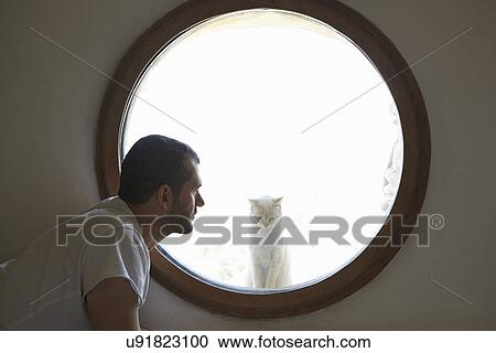 Mid adult man gazing at cat through circular window View Large Photo Image Stock Image - Mid adult man gazing at cat through circular window. Fotosearch
