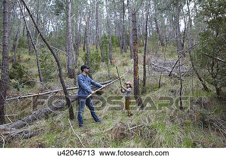Stock Image - Mid adult man play fighting with daughter in forest. Fotosearch