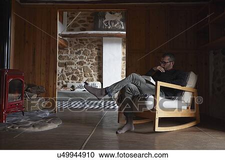 Stock Image - Mid adult man reading book in sitting room. Fotosearch
