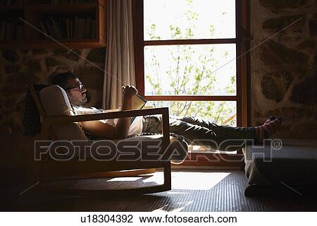 Mid adult man reading book whilst relaxing in sitting room View Large Photo Image Stock Image - Mid adult man reading book whilst relaxing in sitting room. Fotosearch