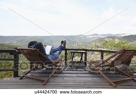 Stock Image - Mid adult man relaxing with book on balcony, Villahermosa del Rio, Castellon, Spain. Fotosearch