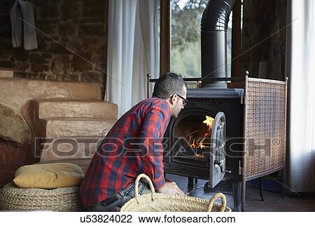 Stock Image - Mid adult man watching log burning fire. Fotosearch