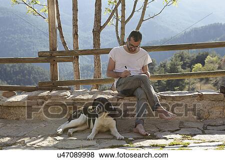 Stock Photo - Mid adult man with dog writing notes on patio. Fotosearch