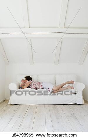 Stock Photography - Mid adult mother lying on sofa and kissing baby daughter. Fotosearch
