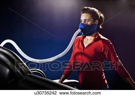 Stock Image - Mid adult woman with face mask on gym treadmill in altitude centre. Fotosearch