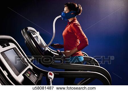 Stock Photo - Mid adult woman with face mask running on gym treadmill in altitude centre. Fotosearch