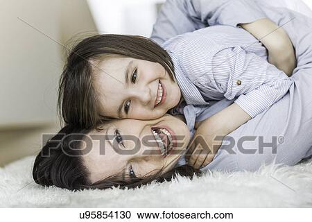 Stock Image - Mother and daughter lying on rug, laughing. Fotosearch