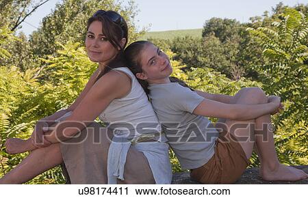 Mother and daughter sitting back to back in garden View Large Photo Image Stock Image - Mother and daughter sitting back to back in garden. Fotosearch