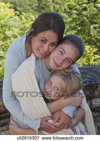 Stock Photo - Mother and daughters in garden, hugging. Fotosearch