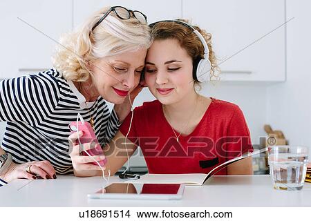 Mother and teenage daughter listening to music on headphones at home View Large Photo Image Picture - Mother and teenage daughter listening to music on headphones at home. Fotosearch