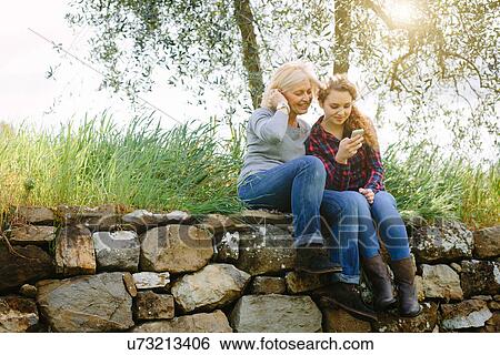 Mother and teenage daughter looking at smartphone on dry stone wall View Large Photo Image Stock Photograph - Mother and teenage daughter looking at smartphone on dry stone wall. Fotosearch