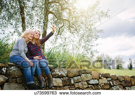 Stock Image - Mother and teenage daughter taking self portrait on dry stone wall. Fotosearch