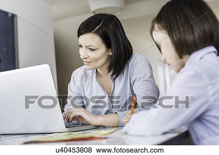 Mother using laptop, daughter writing View Large Photo Image Stock Photo - Mother using laptop, daughter writing. Fotosearch