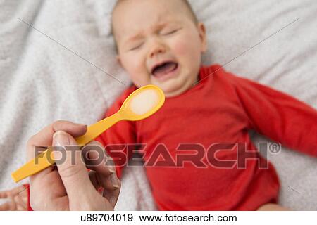 Stock Photo - Mothers hand holding spoon to feed crying baby daughter. Fotosearch