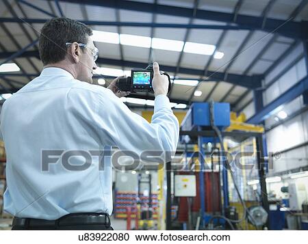 Stock Image - Office worker using infra red camera to check power use in factory. Fotosearch