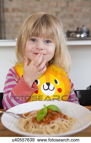 Stock Photo - Portrait of 2 year old girl eating spaghetti with fingers. Fotosearch